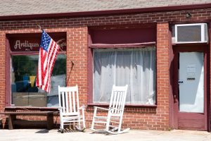 Two rocking chairs and an American flag in front of a small town antique store